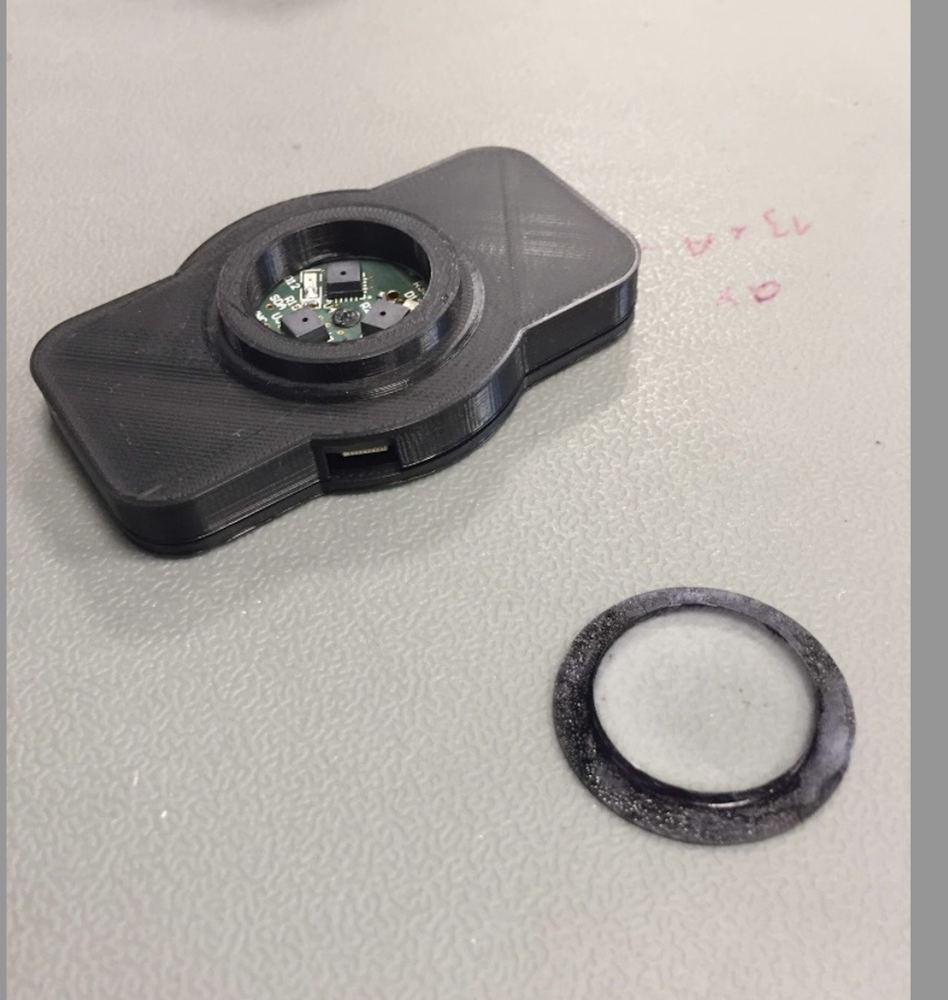A 3D-printed sensor housing with the circuit board inside, next to a felt sealing ring.